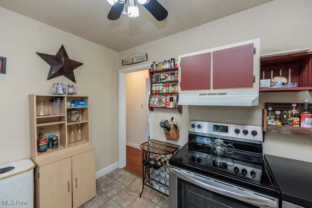 Kitchen featuring open shelves, stainless steel range with electric cooktop, a ceiling fan, stone finish floors, and under cabinet range hood