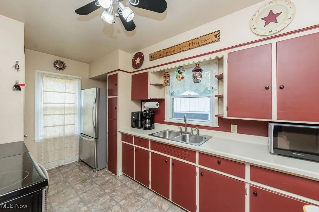 Kitchen featuring red cabinetry, freestanding refrigerator, black electric range oven, ceiling fan, and healthy amount of natural light