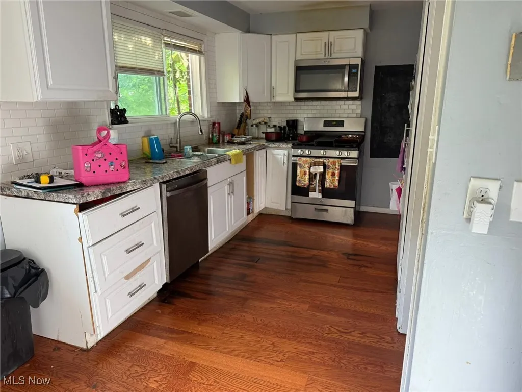 Kitchen with appliances with stainless steel finishes, white cabinetry, tasteful backsplash, and dark wood-style flooring