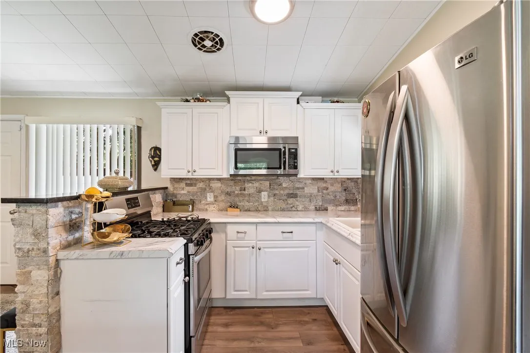 Kitchen featuring stainless steel appliances, dark wood-style floors, light countertops, backsplash, and white cabinetry