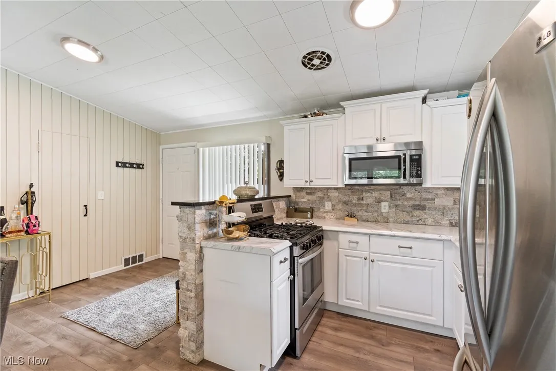 Kitchen with stainless steel appliances, a peninsula, white cabinetry, tasteful backsplash, and wood finished floors