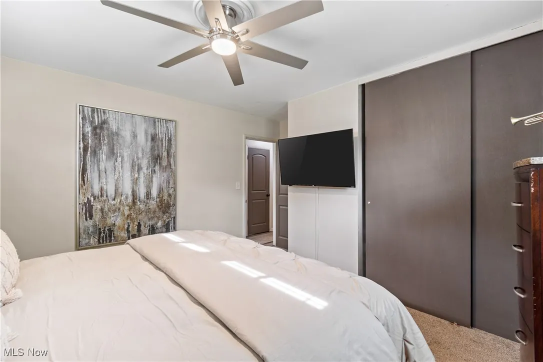 Carpeted bedroom with ceiling fan and a closet