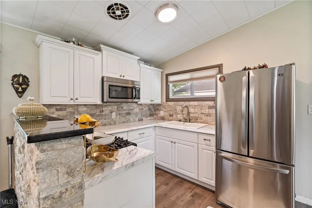Kitchen featuring appliances with stainless steel finishes, white cabinetry, decorative backsplash, wood finished floors, and light countertops