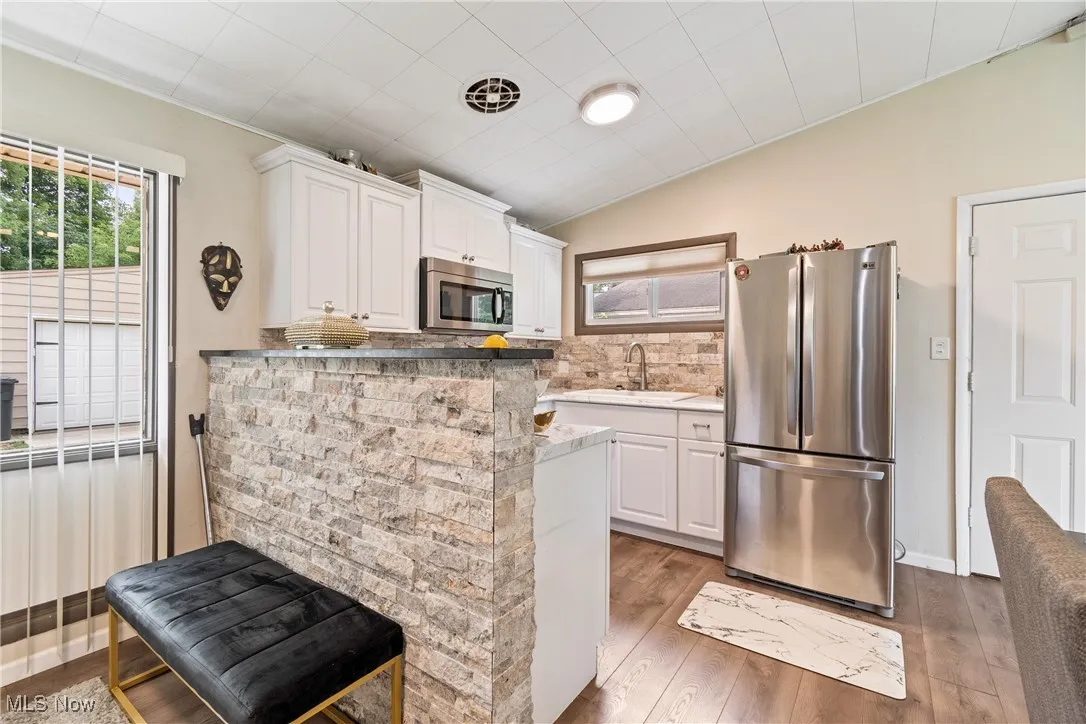 Kitchen with appliances with stainless steel finishes, light wood finished floors, white cabinetry, backsplash, and lofted ceiling