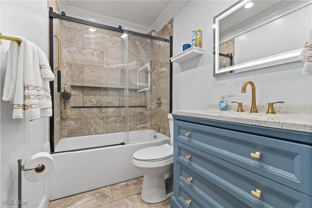 Full bathroom featuring vanity, combined bath / shower with glass door, crown molding, and stone finish floors