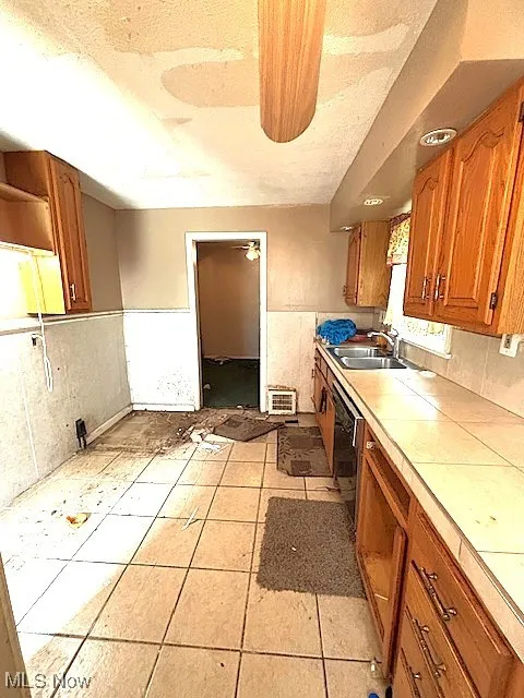 Kitchen with tile countertops, brown cabinetry, and black dishwasher
