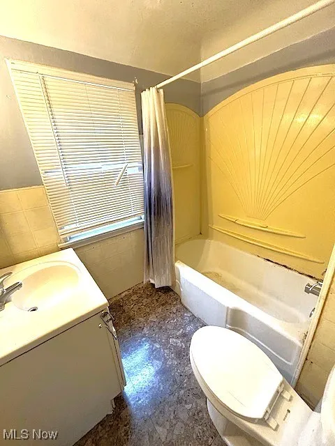 Full bathroom featuring shower / bath combination with curtain, tile walls, vanity, and a wainscoted wall