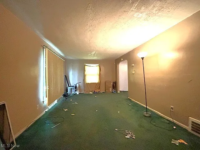 Carpeted spare room featuring a textured ceiling and baseboards