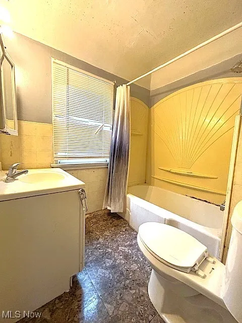 Full bath with vanity, tile walls, shower / bath combo with shower curtain, and wainscoting