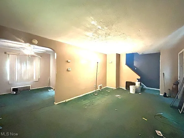 Additional living space featuring arched walkways, carpet, and a ceiling fan
