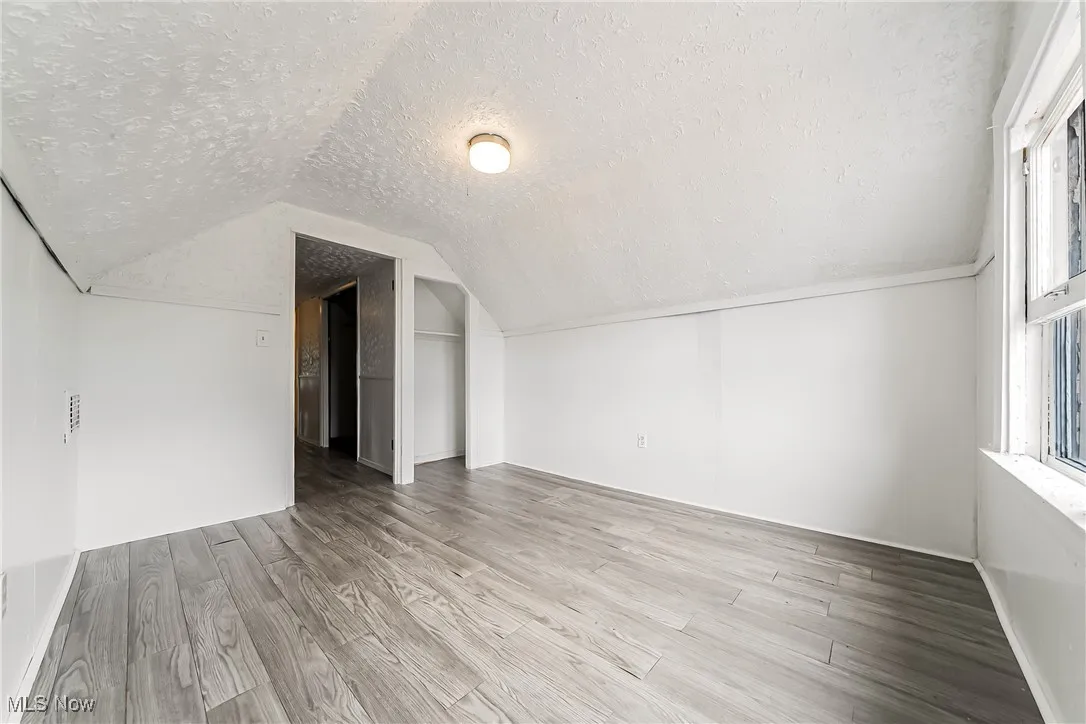 Additional living space featuring a textured ceiling, wood finished floors, and vaulted ceiling