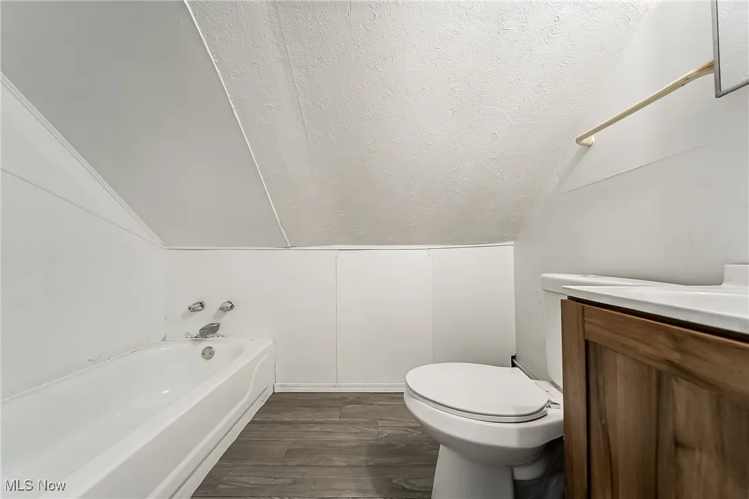 Full bath featuring lofted ceiling, vanity, a textured ceiling, wood finished floors, and washtub / shower combination