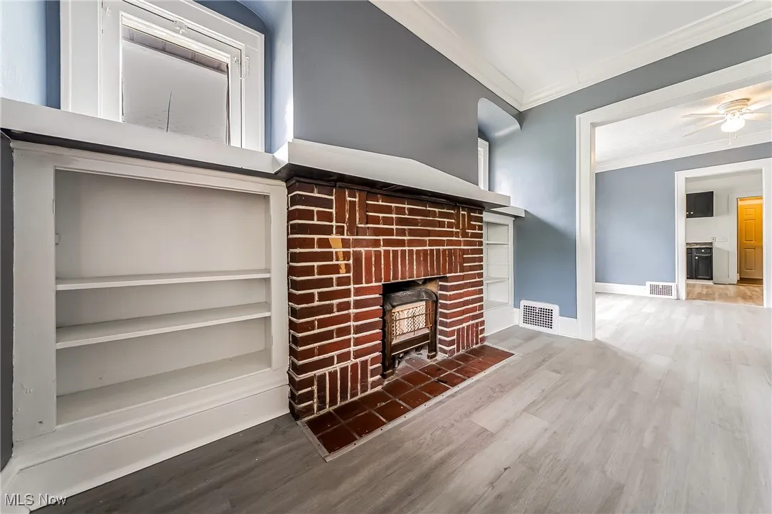 Unfurnished living room featuring crown molding, a brick fireplace, wood finished floors, and ceiling fan