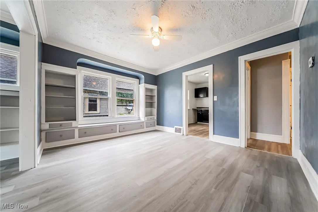 Unfurnished bedroom with a textured ceiling, wood finished floors, crown molding, ceiling fan, and ensuite bath