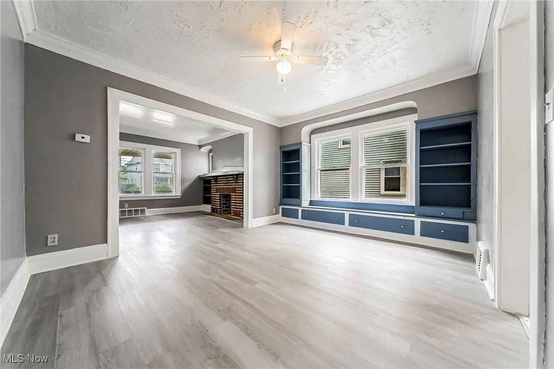 Unfurnished living room with light wood-style flooring, ornamental molding, a ceiling fan, a textured ceiling, and built in features