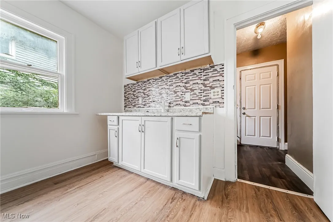 Kitchen with light wood-style floors, decorative backsplash, white cabinets, and light stone countertops