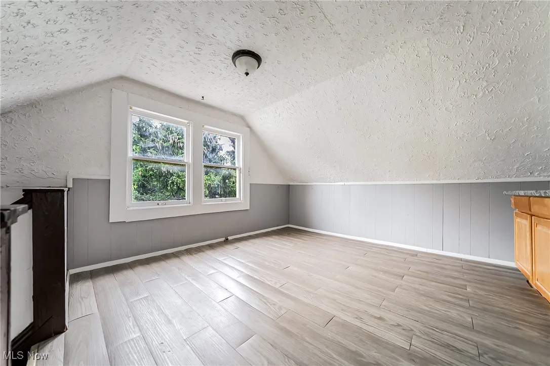 Additional living space with a textured ceiling, wood finished floors, and vaulted ceiling