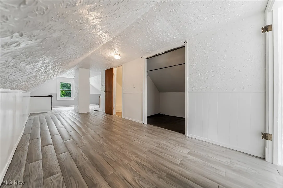 Bonus room with wood finished floors, a textured ceiling, lofted ceiling, and wainscoting