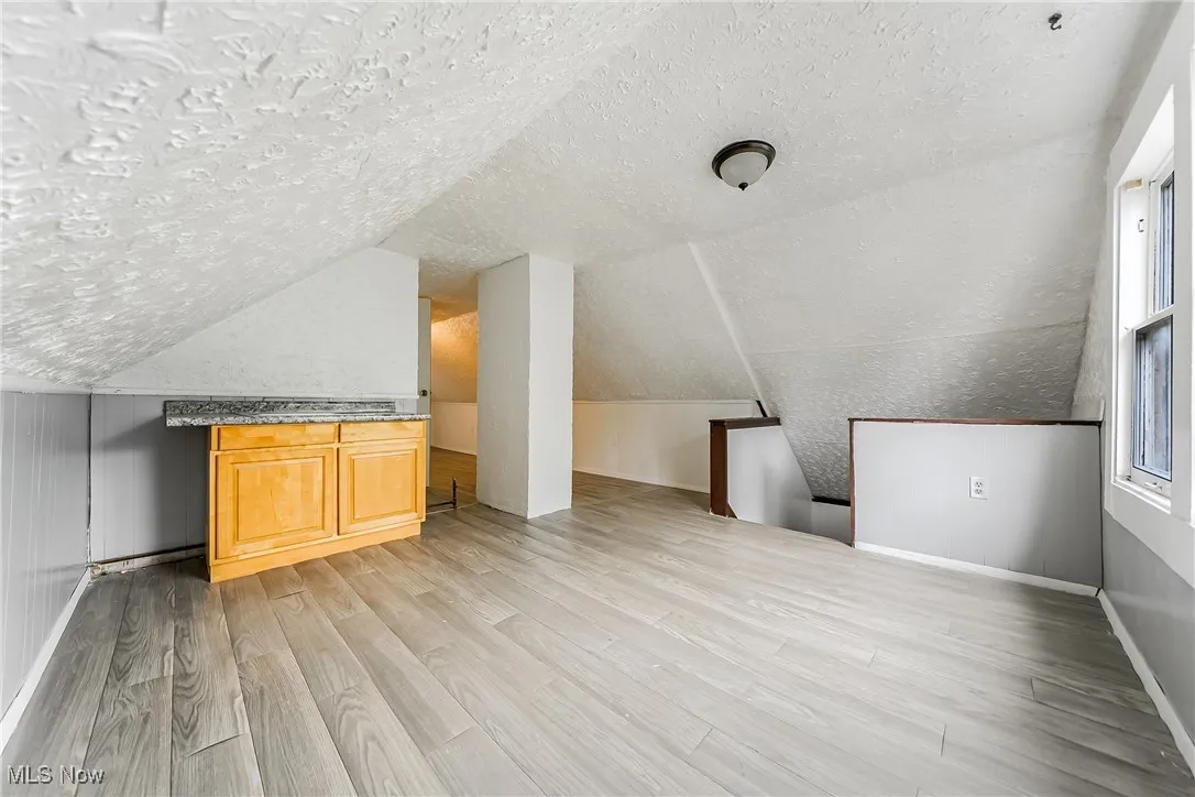 Bonus room featuring a textured ceiling, light wood finished floors, and vaulted ceiling