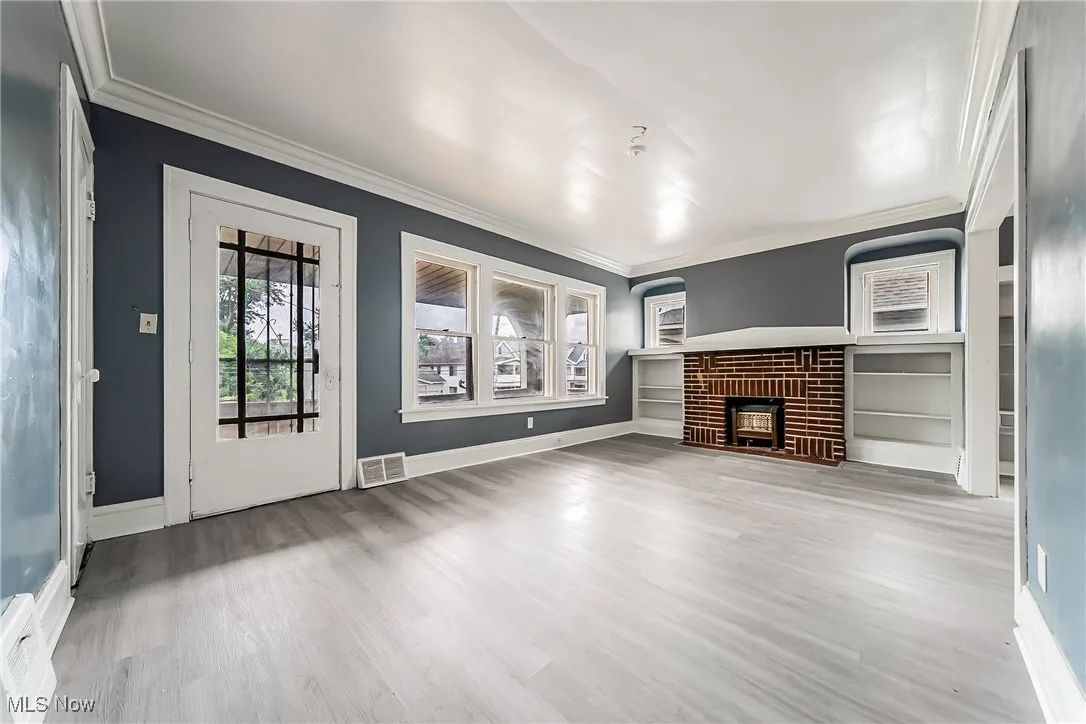 Unfurnished living room with crown molding, a fireplace, wood finished floors, and built in features