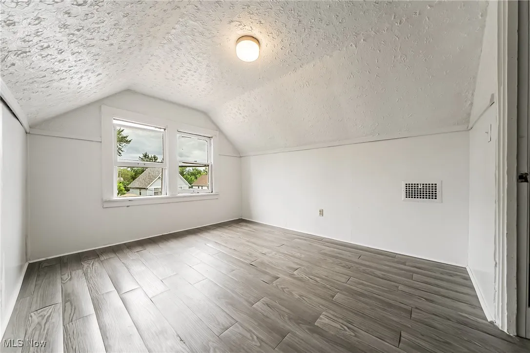 Additional living space with a textured ceiling, wood finished floors, and vaulted ceiling
