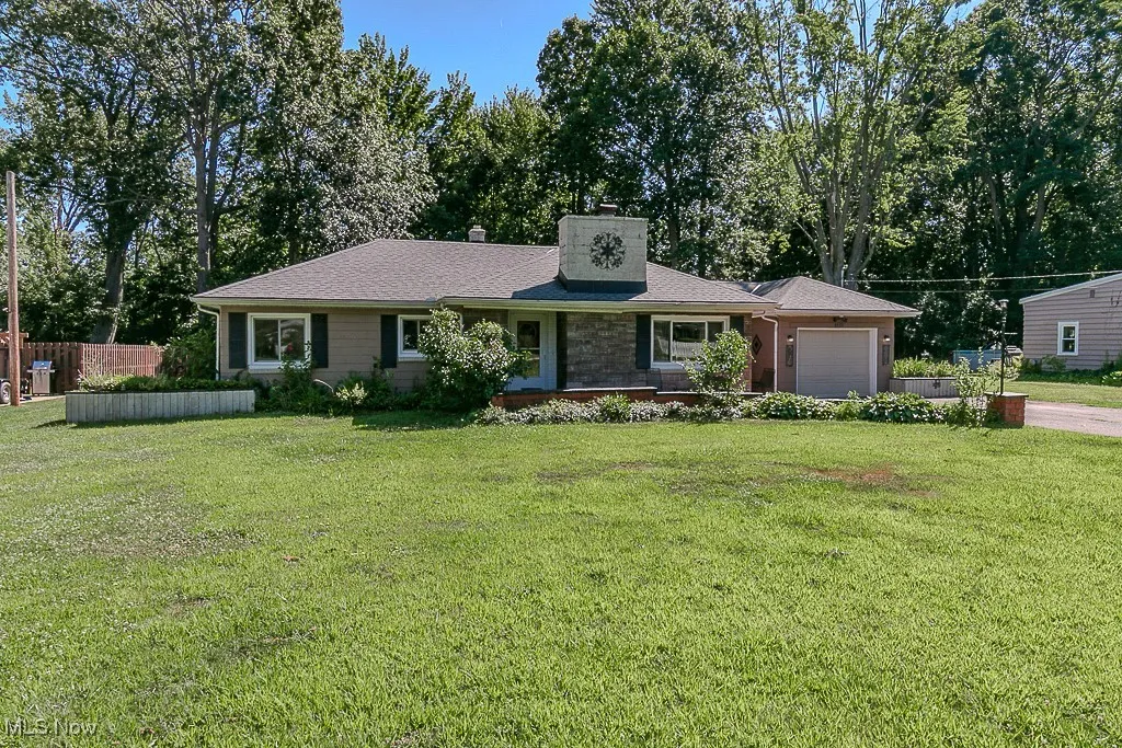 Ranch-style home featuring a chimney, an attached garage, roof with shingles, and driveway