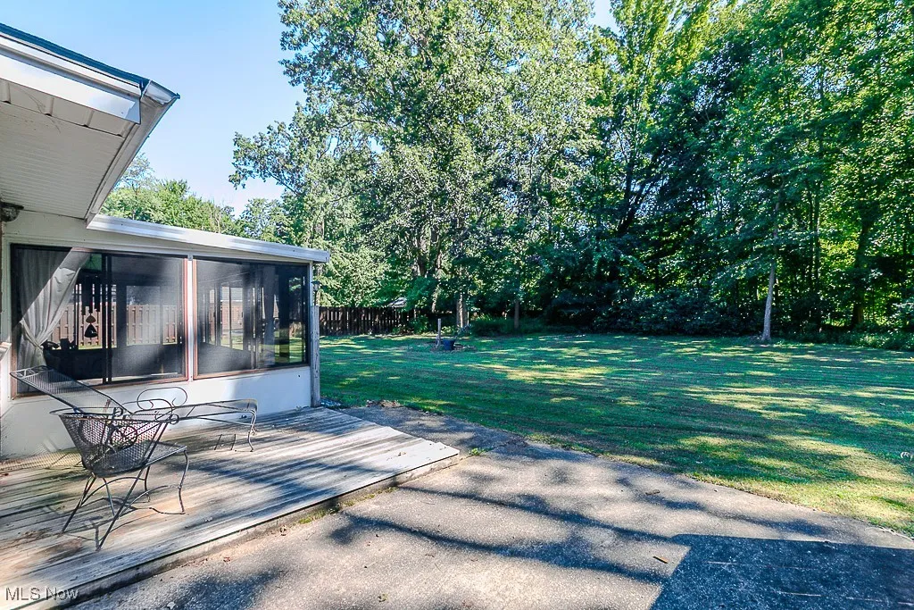 View of green lawn with a sunroom and a wooden deck