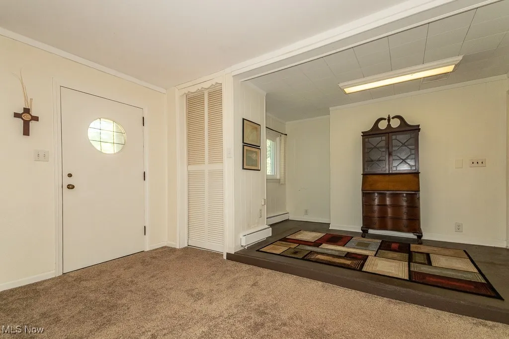 Entrance foyer with ornamental molding, carpet flooring, and baseboard heating