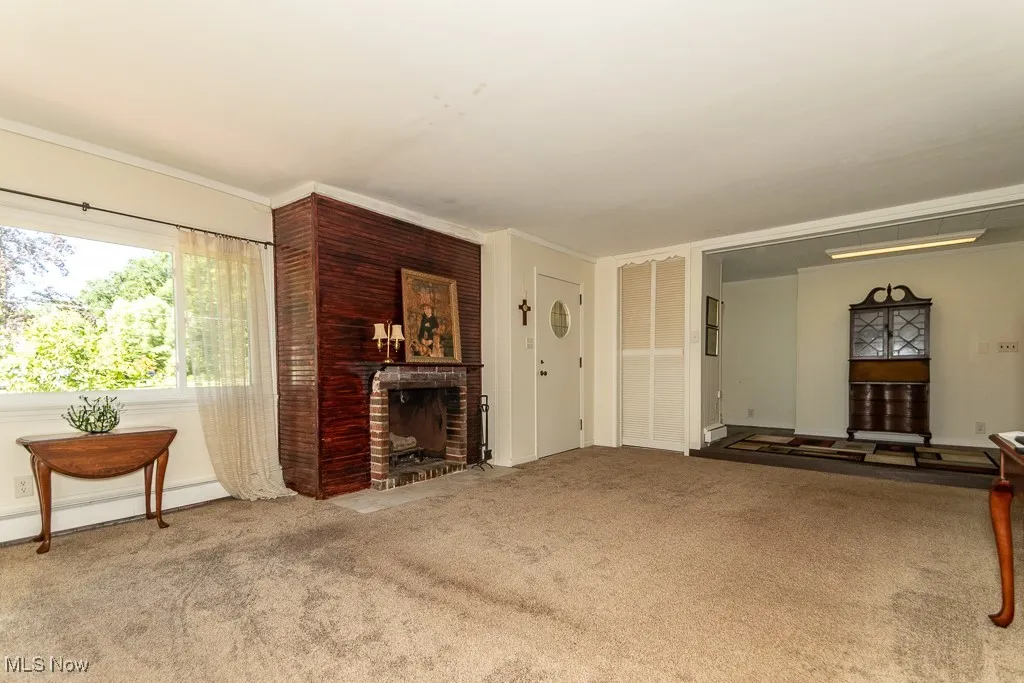 Unfurnished living room with a brick fireplace, carpet floors, and crown molding