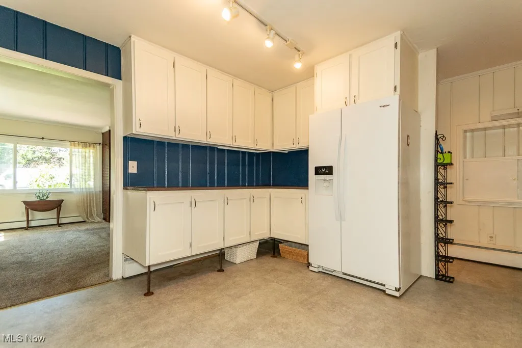 Kitchen with white fridge with ice dispenser, white cabinetry, light carpet, and baseboard heating