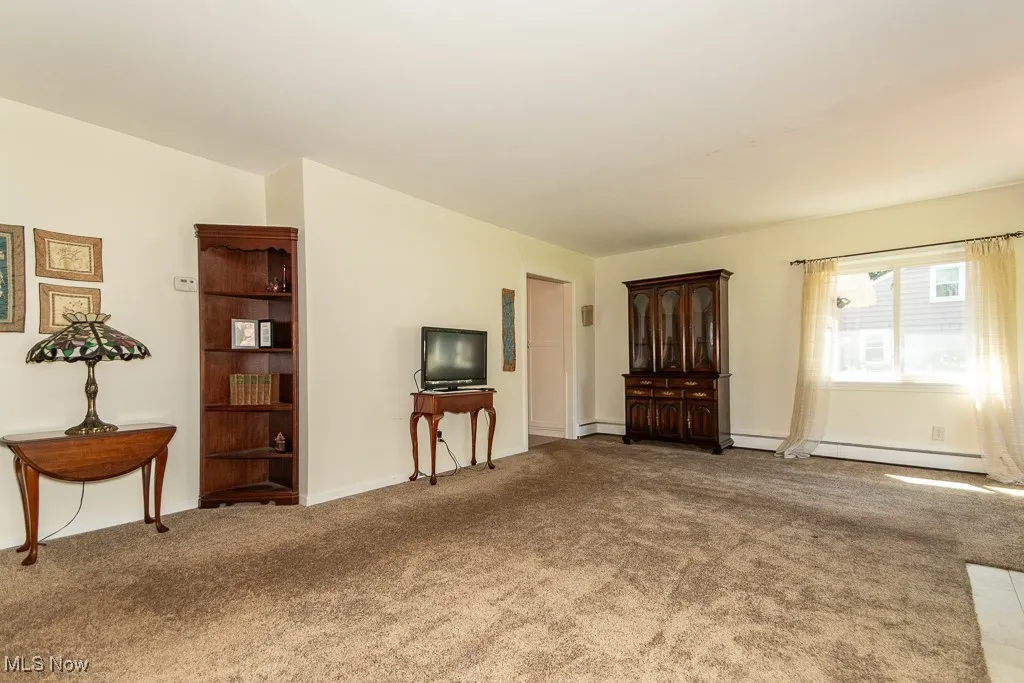 Carpeted living area featuring a baseboard heating unit and baseboards