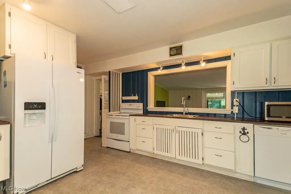 Kitchen featuring white appliances, dark countertops, and white cabinetry