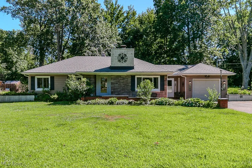 Single story home with an attached garage, a chimney, a shingled roof, a front lawn, and driveway