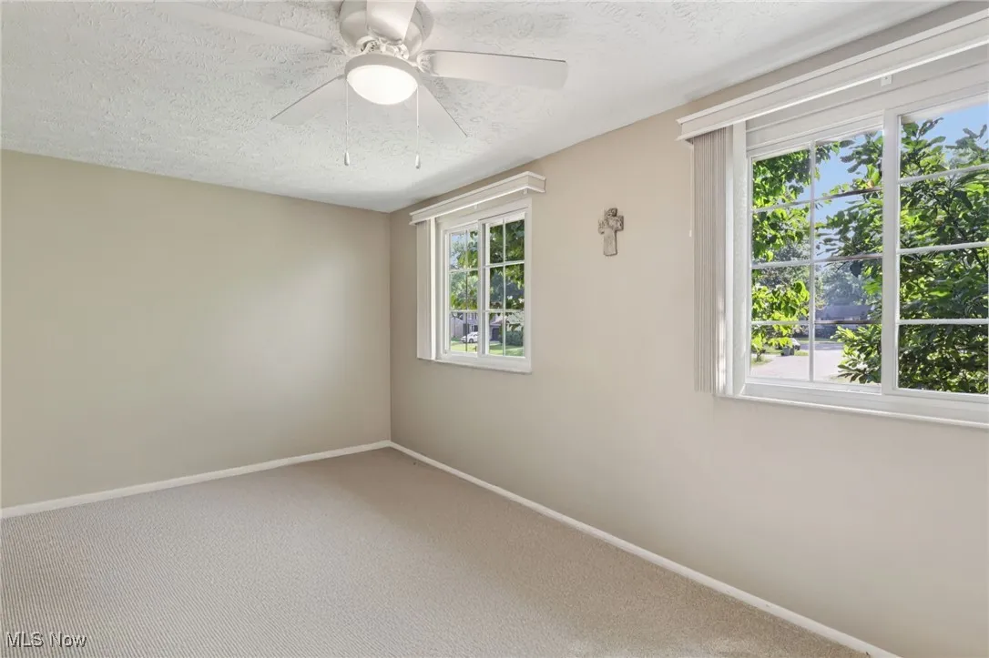 First spacious bedroom with carpet and lighted ceiling fan and windows with custom blinds