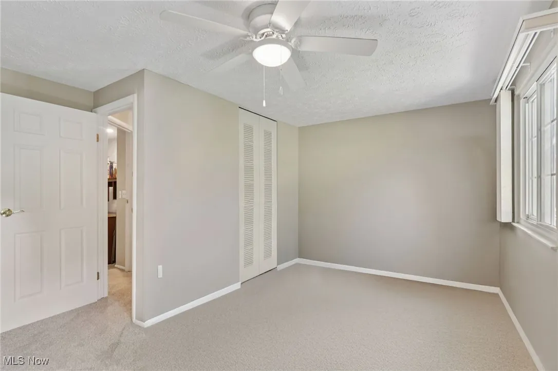 First spacious bedroom with carpet and lighted ceiling fan and windows with custom blinds