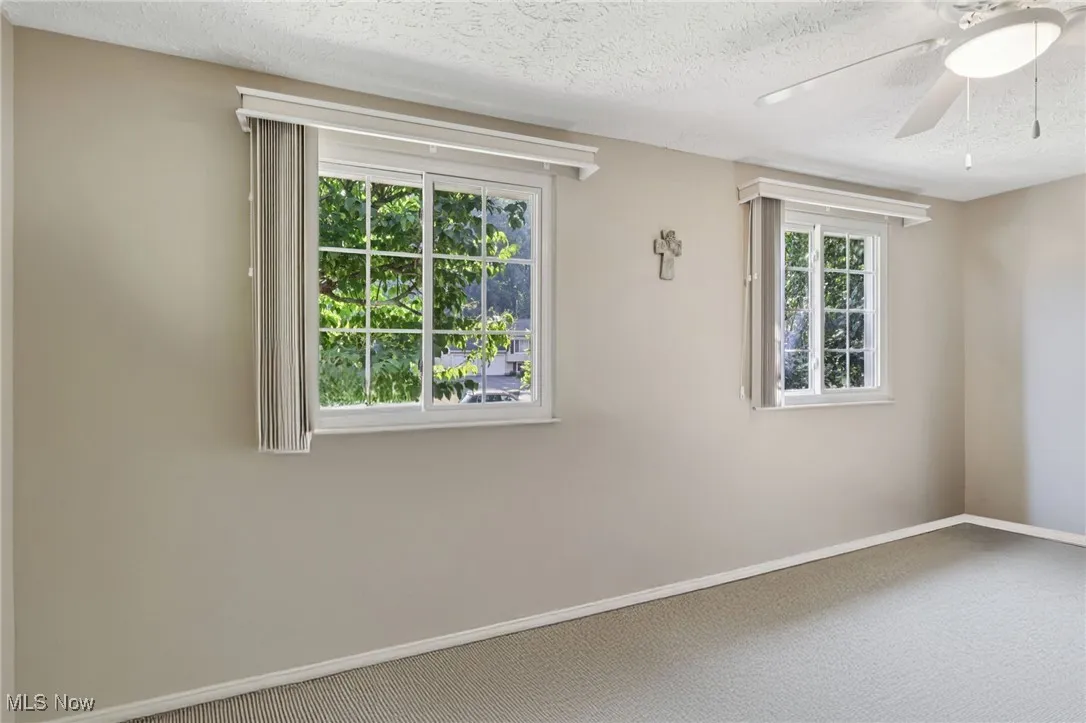 First spacious bedroom with carpet and lighted ceiling fan and windows with custom blinds