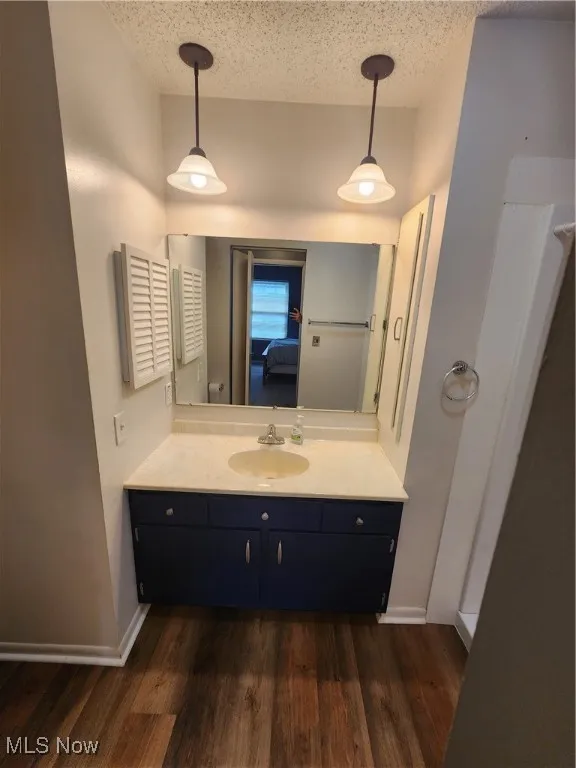 Ensuite bathroom featuring vanity, wood finished floors, and a textured​​‌​​​​‌​​‌‌​‌‌​​​‌‌​‌​‌​‌​​​‌​​ ceiling