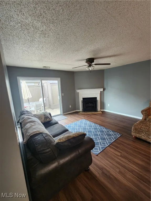 Living room featuring a ceiling fan, wood finished floors, a fireplace, and a textured ceiling