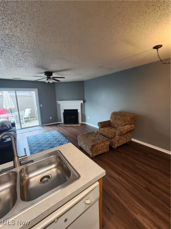 Living room featuring a ceiling fan, dark wood-style flooring, a textured ceiling, and a fireplace
