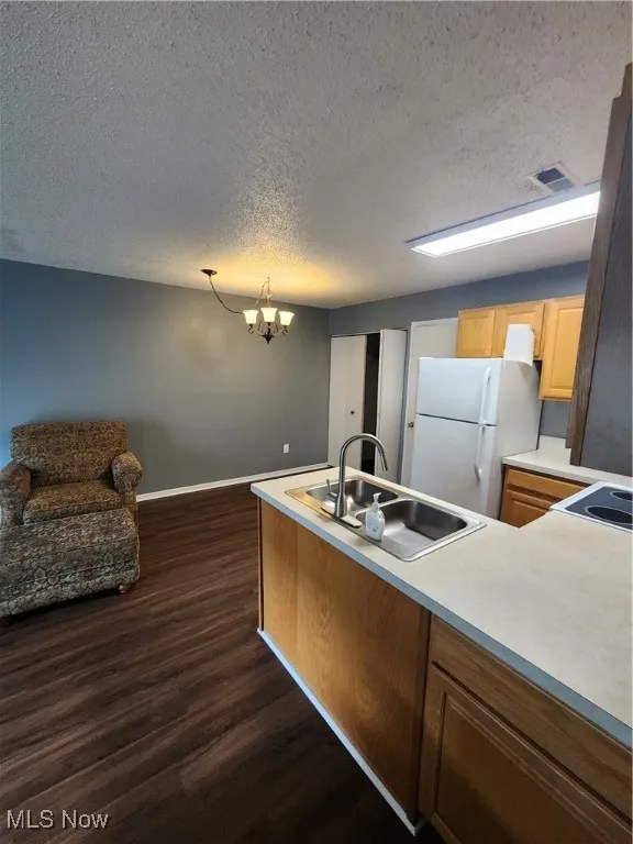 Kitchen with dark wood-style floors, a chandelier, refrigerator, a textured ceiling, and light countertops