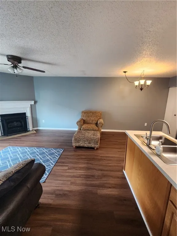 Living room featuring a ceiling fan, a textured ceiling, a fireplace, dark wood-style floors, and a chandelier