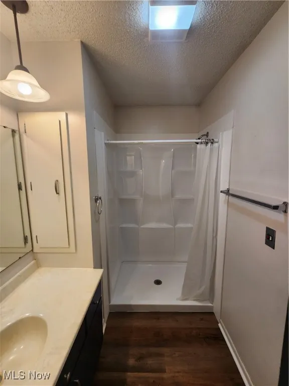 Bathroom featuring a textured ceiling, wood finished floors, vanity, and a shower with curtain