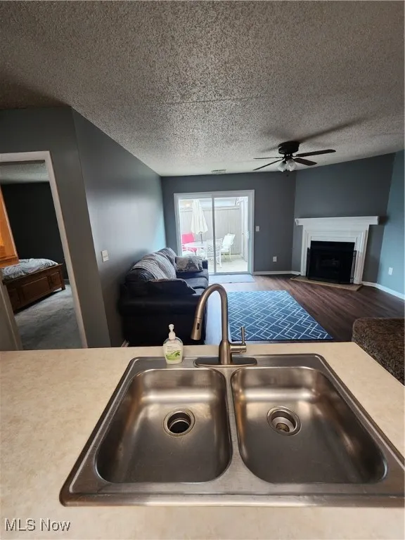 Kitchen view of ceiling fan, wood finished floors, light countertops, a textured ceiling, and a fireplace