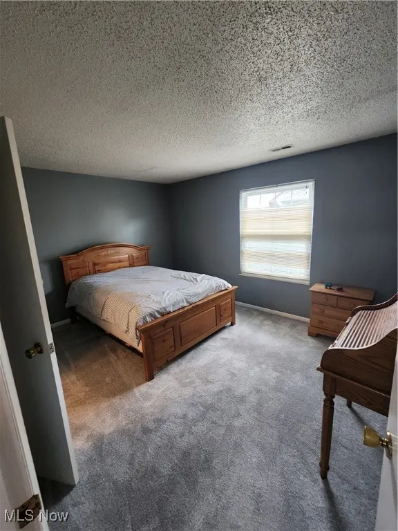 Carpeted bedroom featuring a textured ceiling and baseboards