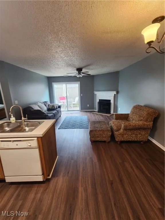 Living area featuring ceiling fan, dark wood-style floors, a fireplace, and a textured ceiling