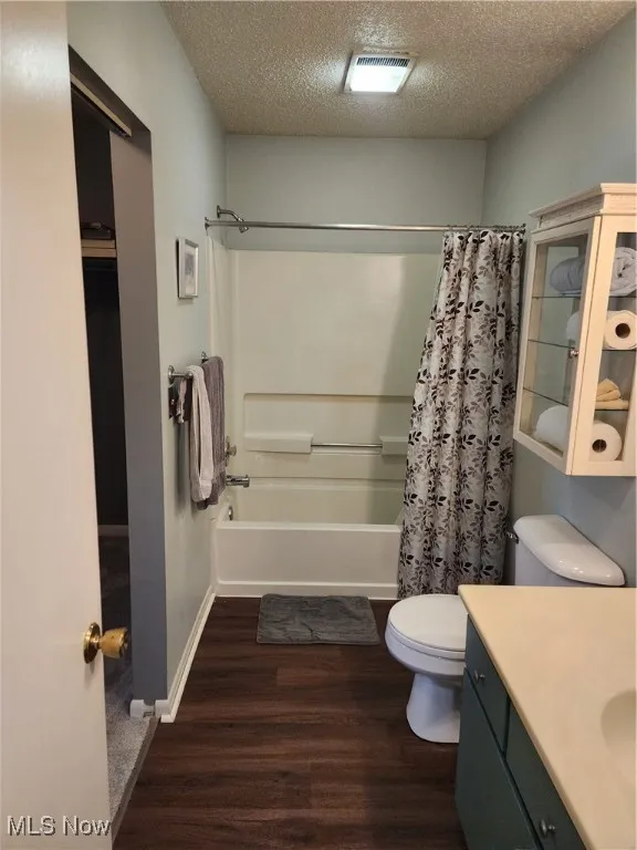Full bath with wood finished floors, shower / bath combo with shower curtain, vanity, and a textured ceiling