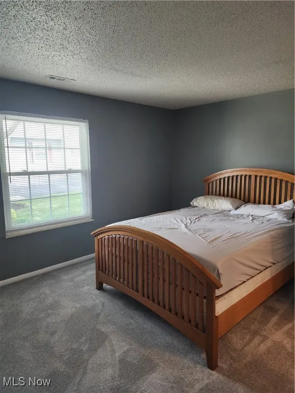 Carpeted bedroom featuring a textured ceiling and baseboards