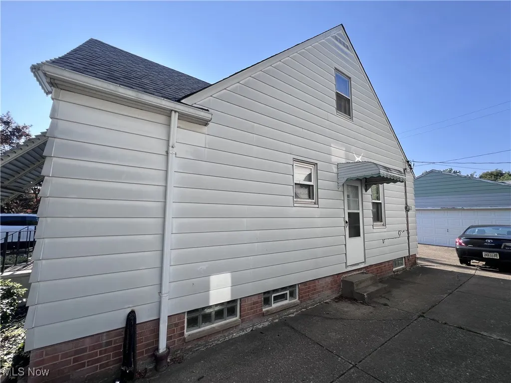 View of side of home featuring roof with shingles, entry steps, an outdoor structure, and a garage