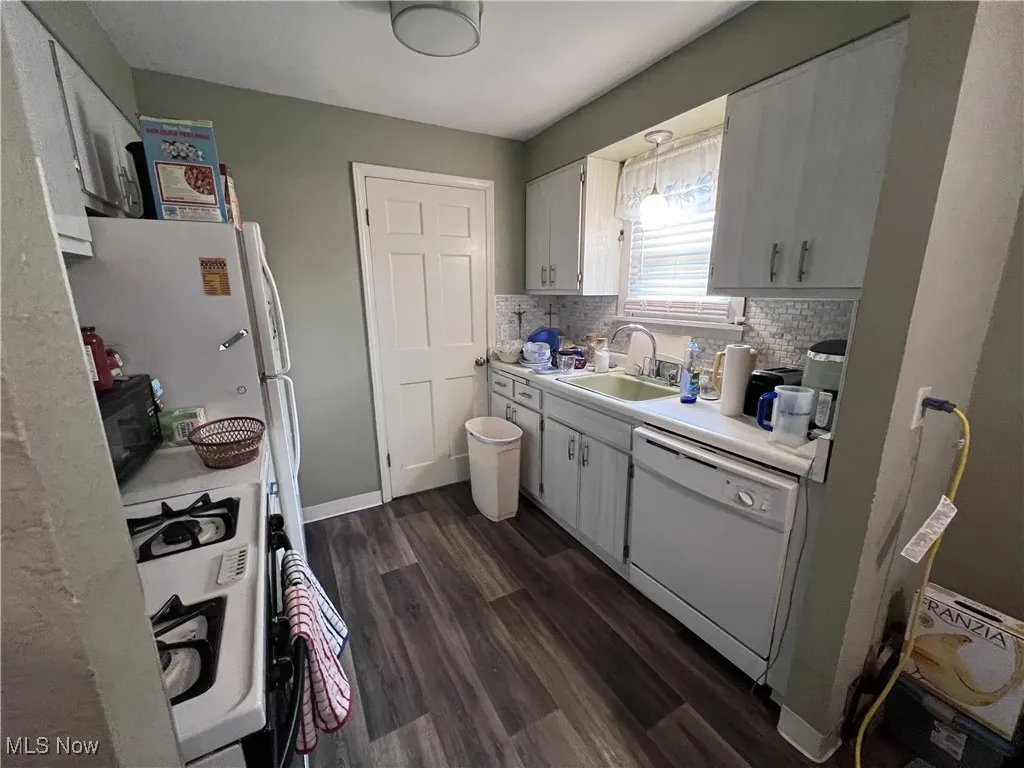 Kitchen featuring light countertops, white appliances, backsplash, and dark wood-style floors