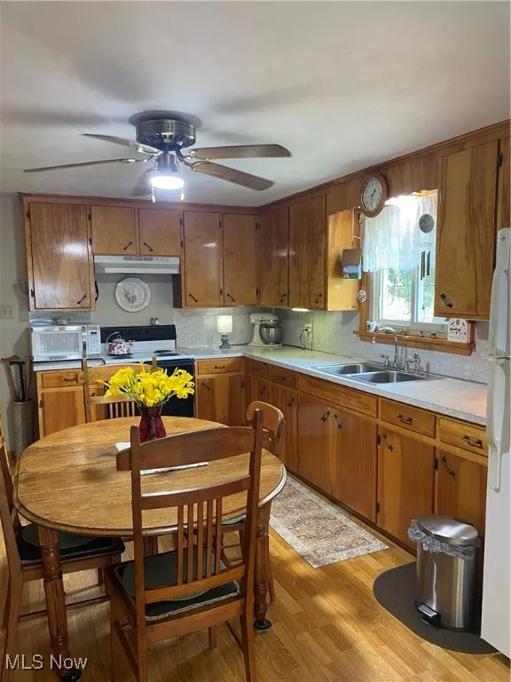 Kitchen featuring light countertops, a ceiling fan, range, light wood-type flooring, and backsplash